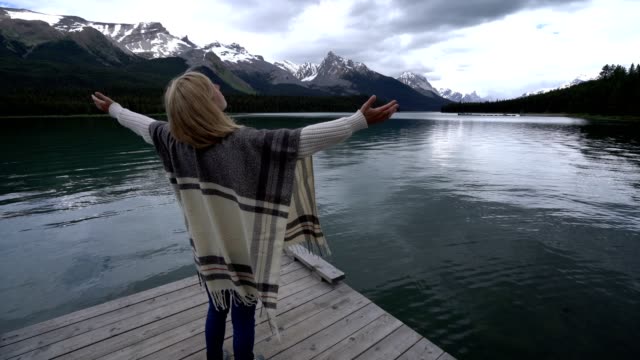 Young-woman-arms-outstretched-on-lake-pier-,-Canada
