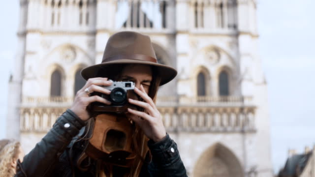 Portrait-of-young-smiling-woman-standing-near-the-Notre-Dame-cathedral-and-taking-photos-on-film-camera-in-Paris,-France