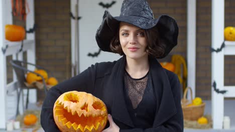 Hübsche-Frau-im-Hexenkostüm-posiert-mit-Halloween-Kürbis