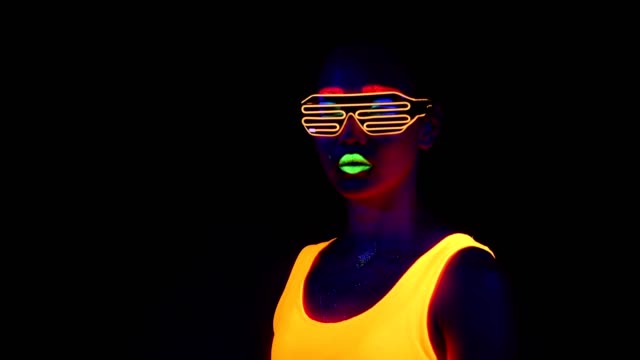 Woman-with-UV-face-paint,-glowing-clothing,-glowing-bracelet,-glasses-in-front-of-camera,-half-body-shot.-Asian-woman.-.