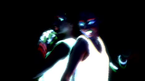 Women-with-UV-face-paint,-glowing-bracelets,-glowing-glasses,-clothing-dancing-back-against-each-other-in-front-of-camera,-Half-body-shot.-Caucasian-and-asian-woman.-Glitch-effect.-Women.
