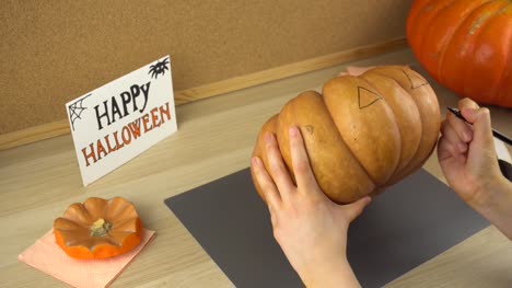 Women's-hands-draw-a-face-on-a-pumpkin-for-Halloween-using-black-felt-tip-pen