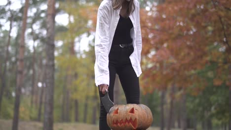 Halloween.-Girl-with-a-butcher's-knife-coming-to-a-pumpkin