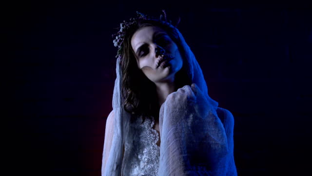 Horror-Halloween-Szene-von-einem-Corpse-Bride-–-Hochzeit-mit-traurigen-Gesicht-und-genähte-Mund-dem-dunklen-Hintergrund-in-die-Kamera-schaut.-Junges-Mädchen-unheimlich-Make-up-steigt-ihre-Hände-versuchen,-berühren-die