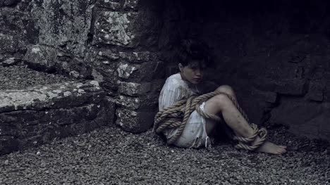 4k-Horror-Shot-of-an-Abandoned-Child-Sitting-on-Rocks-Tied-with-Ropes