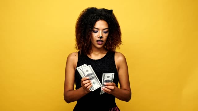Joven-mujer-africana-complicada-contando-dinero-y-ocultar-dinero-aislado-sobre-fondo-amarillo