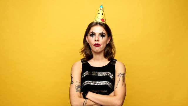 Unhappy-creepy-lady-with-dark-make-up-and-cap-blowing-birthday-horn-isolated-over-yellow