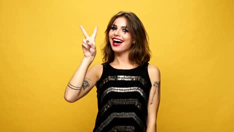 Crazy-cheerful-brunette-woman-with-haloween-make-up-laughing-and-showing-peace-gesture-isolated-over-yellow