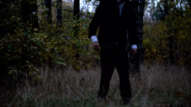 Geheimnisvolle-kopflose-Gestalt-im-Anzug-mit-einem-Schmetterling-im-dunklen-Wald-spazieren,-am-Vorabend-von-halloween