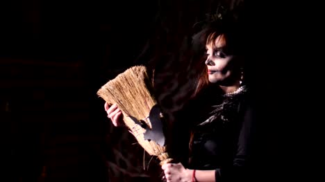 Fiesta-de-Halloween,-noche,-espantoso-retrato-de-una-mujer-en-el-ocaso,-en-los-rayos-de-luz.-mujer-con-un-maquillaje-terrible-en-un-disfraz-de-bruja-negro.-ella-tiene-una-escoba-con-un-bate