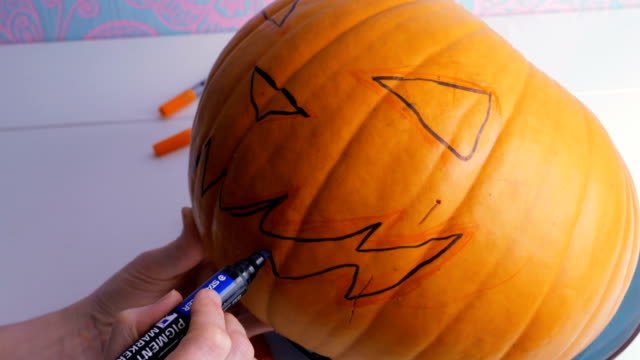 Family-preparing-for-Halloween.-Drawing-a-demon-face-on-a-pumpkin-with-a-marker