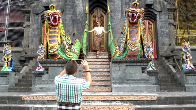 Ein-Mann-nimmt-Bilder-einer-Frau-auf-einem-Smartphone-vor-dem-Eingang-zu-einem-buddhistischen-Tempel