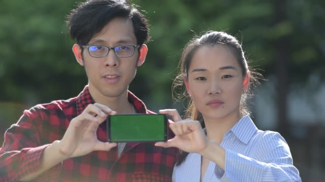 Junge-asiatische-Paar-zeigt-Telefon-zusammen-im-freien
