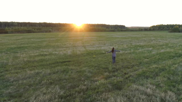 Unrecognizable-woman-walking-on-the-field-at-sunset-arms-outstretched.