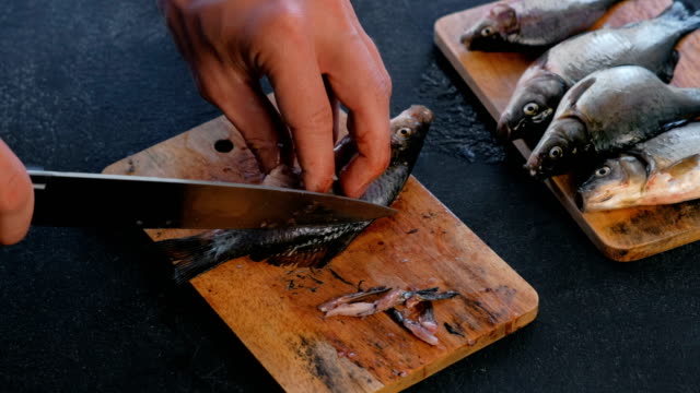 Man-cuts-the-fins-of-the-carp-fish-on-wooden-board.-Cooking-fish.-Hands-close-up.