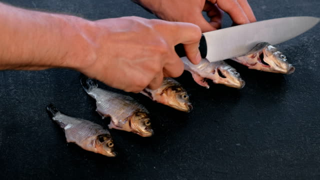 Man-makes-cuts-on-carp-fish-on-black-table.-Cooking-fish.-Close-up-hand.