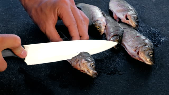 Man-makes-cuts-on-carp-fish-on-black-table.-Cooking-fish.-Close-up-hand.