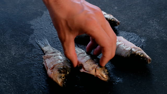 Mann-wendet-sich-der-Karpfen-Fisch-auf-den-Tisch-und-streut-es-mit-Gewürzen.-Fisch-kochen.-Nahaufnahme-der-Hand.