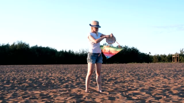 Schöne-Blondine-in-einem-Hut-startet-einen-Kite-am-Strand.