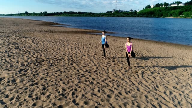 Two-woman-doing-yoga-on-the-beach-by-the-river-in-the-city.-Beautiful-view.-Vrikshasana-pose.