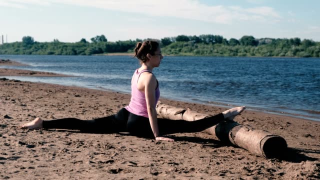 Mujer-haciendo-estiramiento-sentado-en-hilo-en-la-playa-al-atardecer.