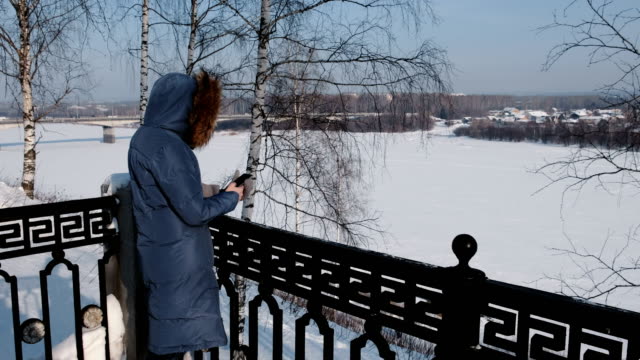 Mujer-irreconocible-en-azul-chaqueta-escribe-mensajes-en-su-teléfono-celular-en-el-parque-de-invierno.