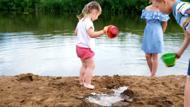 Kleine-Kinder-spielen-im-Fluss-im-Sommer.-Mama-kümmert-sich-um-die-Kinder.