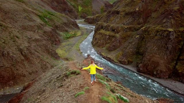 Stunning-drone-view-of-woman-standing-arms-outstretched-on-top-of-canyon-in-Iceland