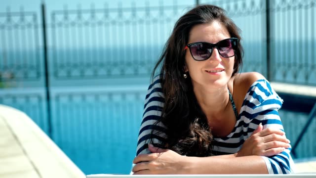 Portrait-happy-smiling-woman-in-sunglasses-enjoying-vacation-lying-on-deck-chair-with-arms-crossed