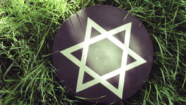 White-Star-of-David-on-a-black-stone-round-on-a-grass-background,-rotation-360-degrees.