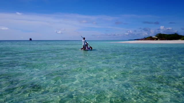 v03861-fliegenden-Drohne-Luftaufnahme-der-Malediven-weißen-Sandstrand-2-Personen-junges-Paar-Mann-Frau-entspannend-auf-Paddleboard-auf-sonnigen-tropischen-Inselparadies-mit-Aqua-blau-Himmel-Meer-Wasser-Ozean-4k