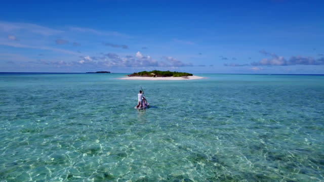 v03859-fliegenden-Drohne-Luftaufnahme-der-Malediven-weißen-Sandstrand-2-Personen-junges-Paar-Mann-Frau-entspannend-auf-Paddleboard-auf-sonnigen-tropischen-Inselparadies-mit-Aqua-blau-Himmel-Meer-Wasser-Ozean-4k