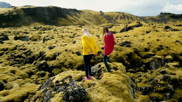 Luftaufnahme-von-zwei-Frauen-stehen-auf-dem-Felsen,-auf-der-Suche-auf-das-Lavafeld-in-Island-und-tanzen,-fühle-mich-glücklich,-Freiheit,