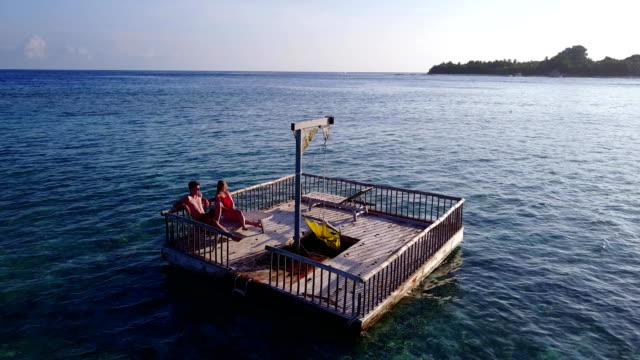 v03845-fliegenden-Drohne-Luftaufnahme-der-Malediven-weißen-Sandstrand-2-Personen-junges-Paar-Mann-Frau-entspannend-auf-sonnigen-tropischen-Inselparadies-mit-Aqua-blau-Himmel-Meer-Wasser-Ozean-4k-schwimmenden-Ponton-Steg-Sonnenbaden-zusammen