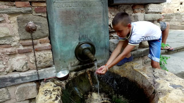 niño-beber-agua-y-lavarse-las-manos-de-grifo-oriental-antiguas-en-la-ciudad-antigua-de-Nesebar,-Bulgaria