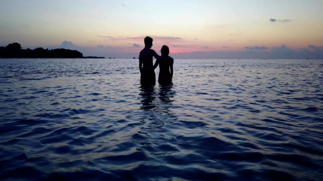 v04178-vuelo-drone-vista-aérea-de-Maldivas-playa-2-personas-pareja-hombre-mujer-amor-romántico-puesta-de-sol-salida-del-sol-en-la-isla-de-paraíso-tropical-soleado-con-cielo-azul-aqua-agua-mar-4k
