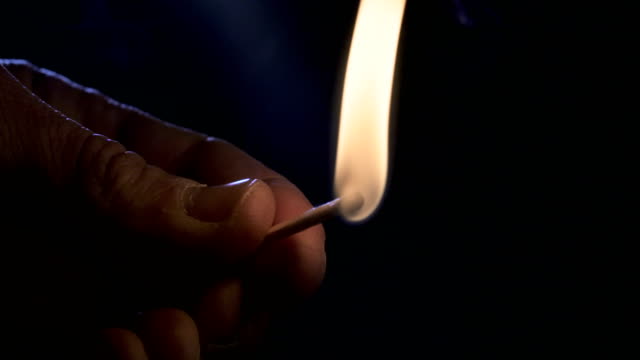 Slow-motion-macro-footage-of-a-white-candle-lit-by-a-match-on-a-dark-background