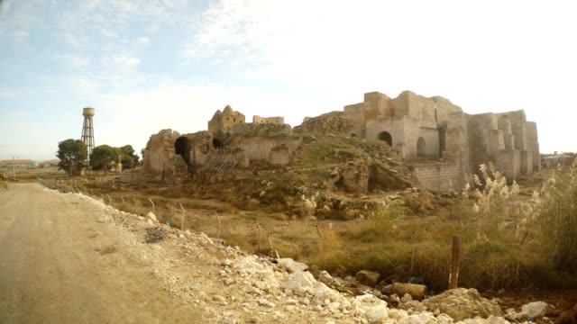 un-motociclista-paseos-a-través-de-una-calle-al-lado-de-un-castillo-medieval-en-ruinas-de-la-aldea-en-el-sureste-de-Turquía