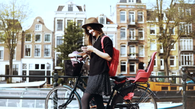 Señora-de-blogger-con-bicicleta-en-un-viejo-puente-de-la-ciudad.-Tipos-de-turista-europeo,-mira-alrededor-disfrutando-día-soleado-caliente.-4K