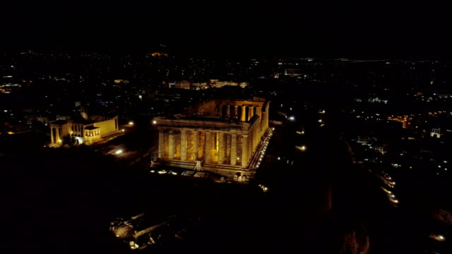 Video-de-noche-aérea-emblemática-antigua-colina-de-la-Acrópolis-y-el-Partenón-por-la-noche,-el-centro-histórico-de-Atenas