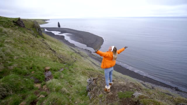Young-woman-arms-outstretched-at-Hvitserkur-basalt-stack-along-the-eastern-shore-of-the-Vatnsnes-peninsula,-in-northwest-Iceland.-People-travel-lifestyles-concept