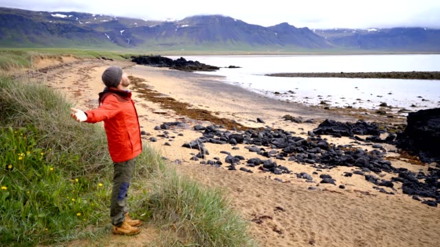 4K-joven-en-soportes-de-Islandia-encima-de-los-brazos-de-una-playa-tendida-de-la-libertad