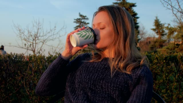 blonde-woman-is-drinking-coffee-from-cardboard-cup-in-sunset-time-in-spring