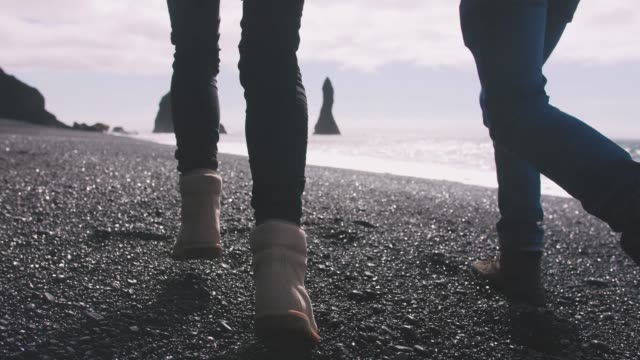Close-up-shot-of-young-couple-holding-hands-running-down-black-sand-beach-in-Iceland,-slow-motion
