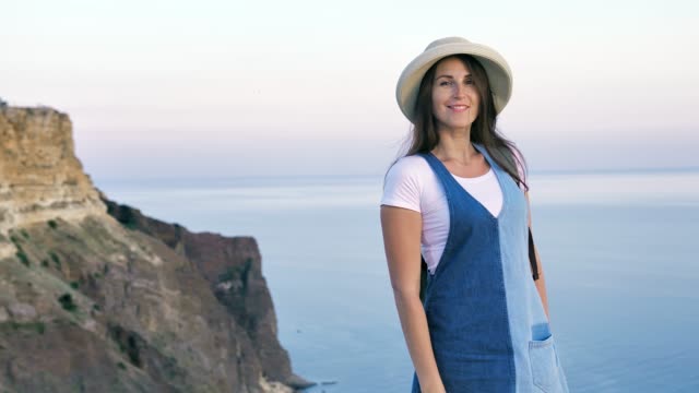 Attractive-elegant-young-woman-in-hat-enjoying-magnificent-sea-and-mountains-at-sunset