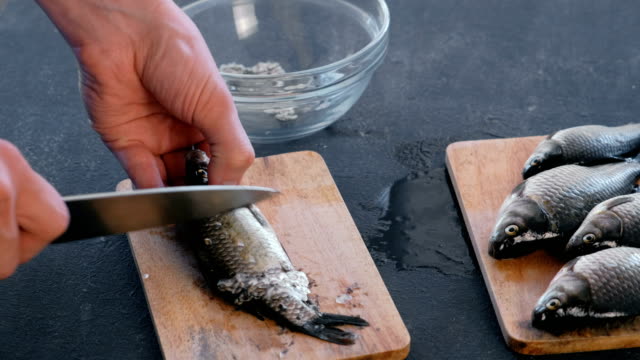 Man-cleans-carp-from-the-scales-on-wooden-board.-Close-up-hands.-Cooking-a-fish.