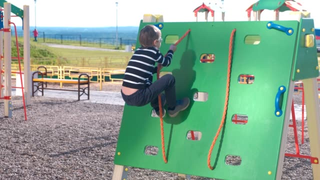 Junge-klettert-auf-eine-Kletterwand-hält-das-Seil-auf-dem-Spielplatz.