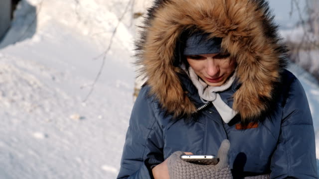 Close-up-Frau-in-blau-Daunenjacke-schreibt-messaging-in-ihr-Handy-in-einem-Winter-Park.-Vorderansicht