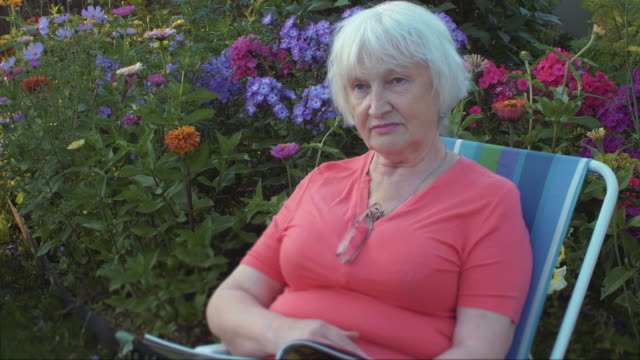 Senior-mujer-leyendo-revista-en-jardín-con-flores-al-aire-libre
