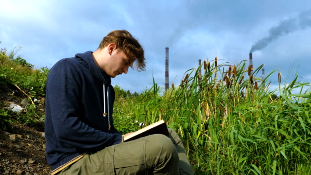 Ein-junger-Mann-sitzt-am-Fluss-und-liest-ein-Buch.
